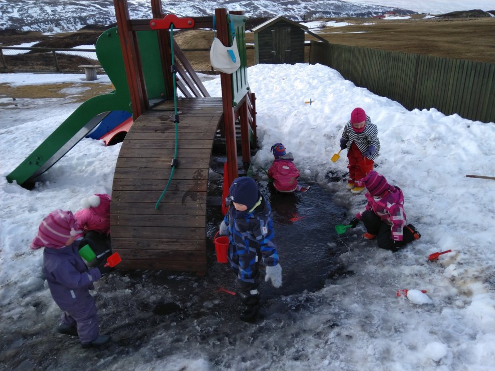 Börnin sækja vatn í pollinn til að selflytja í uppistöðulónið í sandkassanum